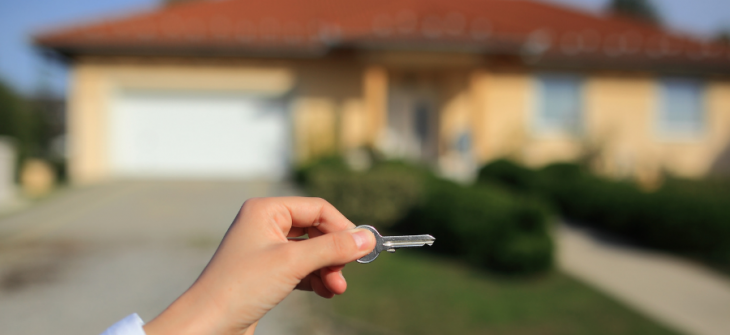 Hand displaying keys in front of a new home